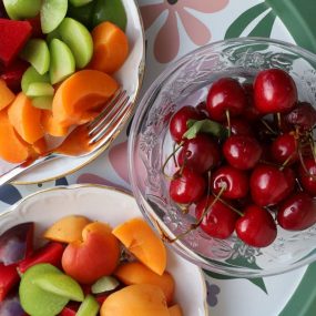 Vibrant mix of fresh summer fruits in decorative bowls on a floral patterned tray.